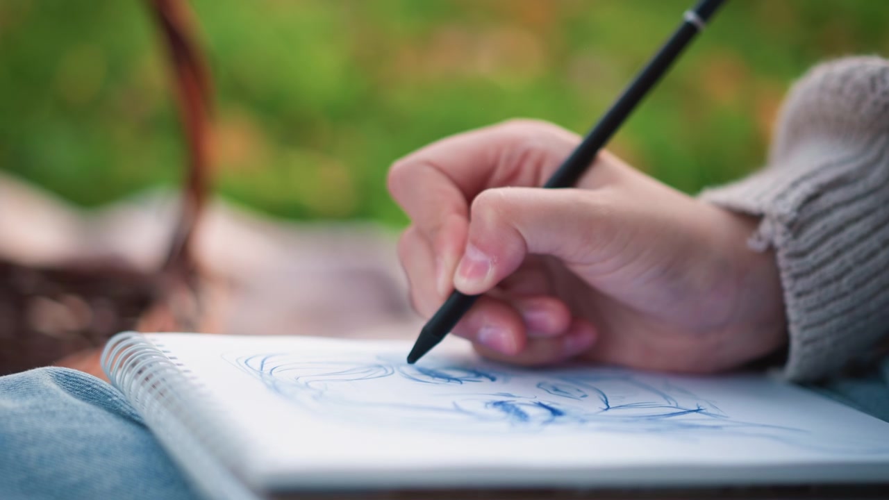 Artista che disegna un personaggio anime su un quaderno a spirale all'aperto.