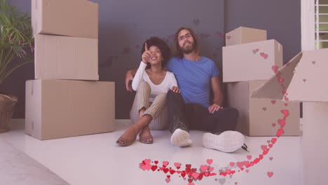 animación de corazones rojos sobre una feliz pareja diversa sentada entre cajas después de mudarse a la casa.
