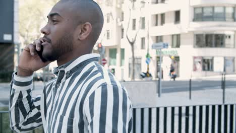 Side-view-of-confident-young-man-talking-on-phone-during-stroll