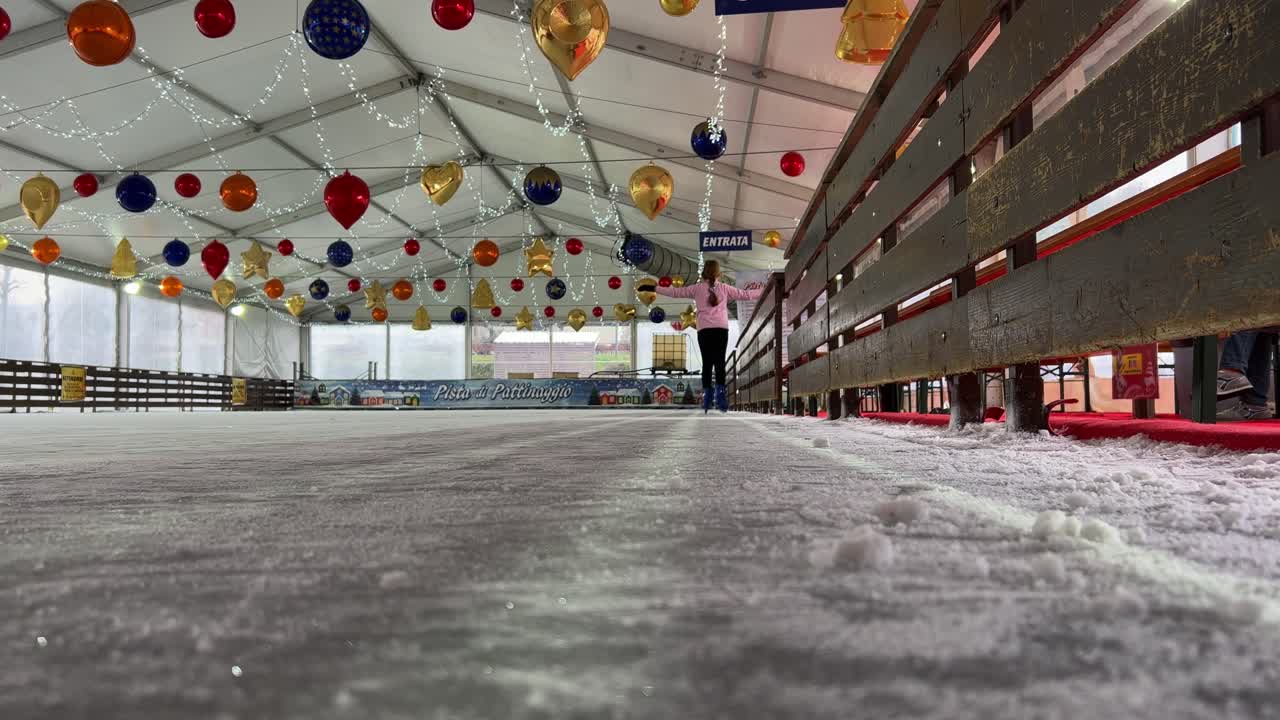 Little cute girl skating on ice alone in empty indoor ice rink with Christmas decorations