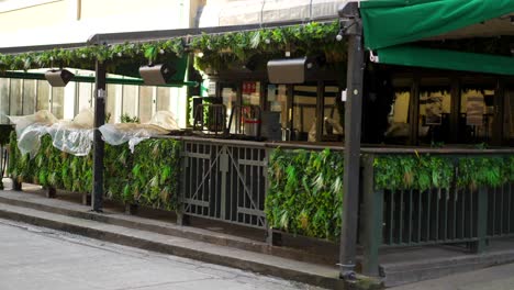 empty terrace of a restaurant or bar, empty tables and seats during covid-19 coronavirus pandemic, no people during lockdown, strong wind blowing on a patio awning and plants, in slow-motion