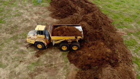 articulated yellow dump truck unloading dirt in field, aerial