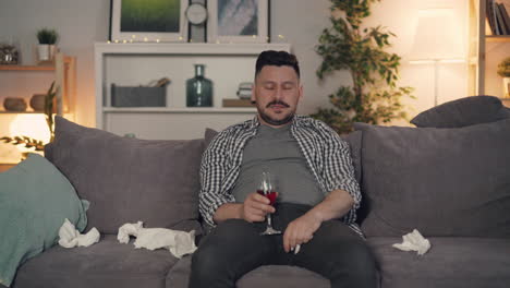 man sitting on couch, drinking wine, looking sad