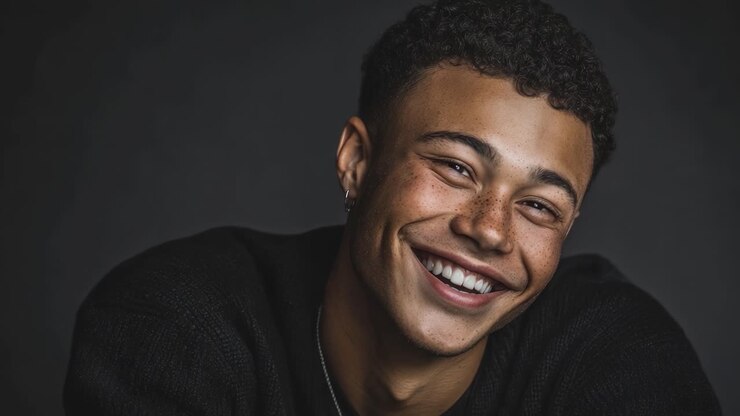 A joyful young man with curly hair and a bright smile radiates happiness and charm in this engaging portrait, showcasing his lively personality and warmth