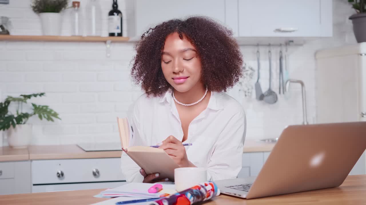 femme afro-américaine réussie prenant des notes dans un carnet de travail en regardant un ordinateur portable