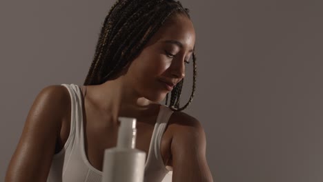 studio skincare beauty shot of young woman with long braided hair putting moisturiser onto arm and shoulder 1