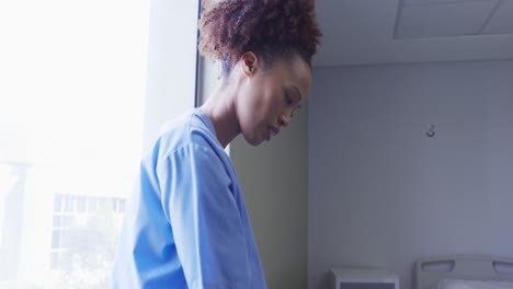 Tired-mixed-race-female-doctor-taking-off-face-mask-standing-in-hospital-room