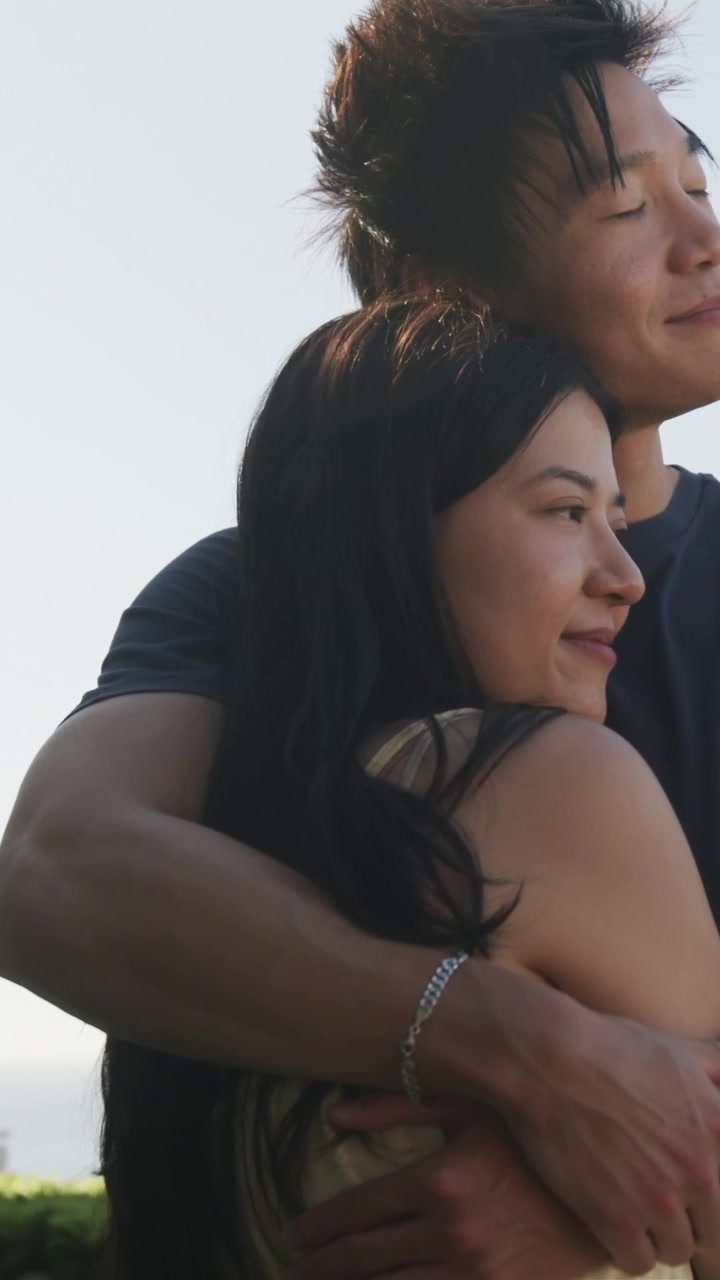 Vertical video: Placing arms, man hugging woman in yellow dress by hedge with bracelet showing love