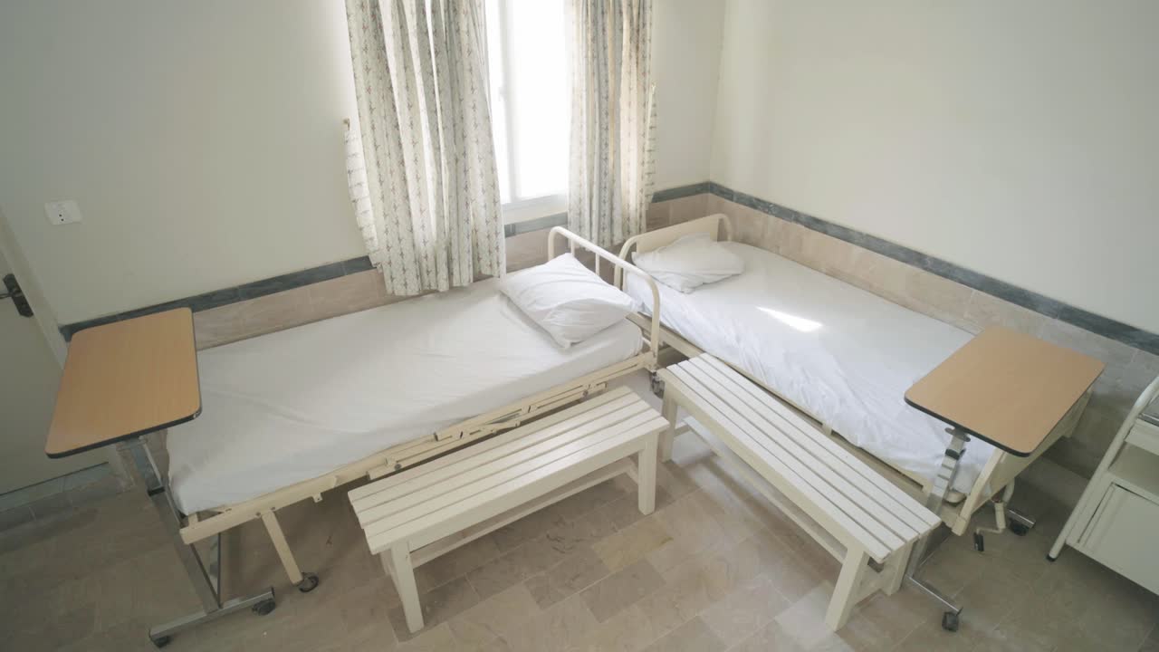 Two empty hospital beds with side tables and benches in a Karachi hospital room, ready for incoming patients