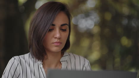 Retrato-Mujer-Seria-Morena-Grupo-étnico-Hispano-Se-Sienta-En-Una-Mesa-En-Un-Café-De-Verano-Con-Una-Computadora-Portátil.-Escribe-En-El-Teclado-Y-Recibe-Capacitación-En-Línea-Compra-Y-Negocia-Con-Un-Banco-De-Internet