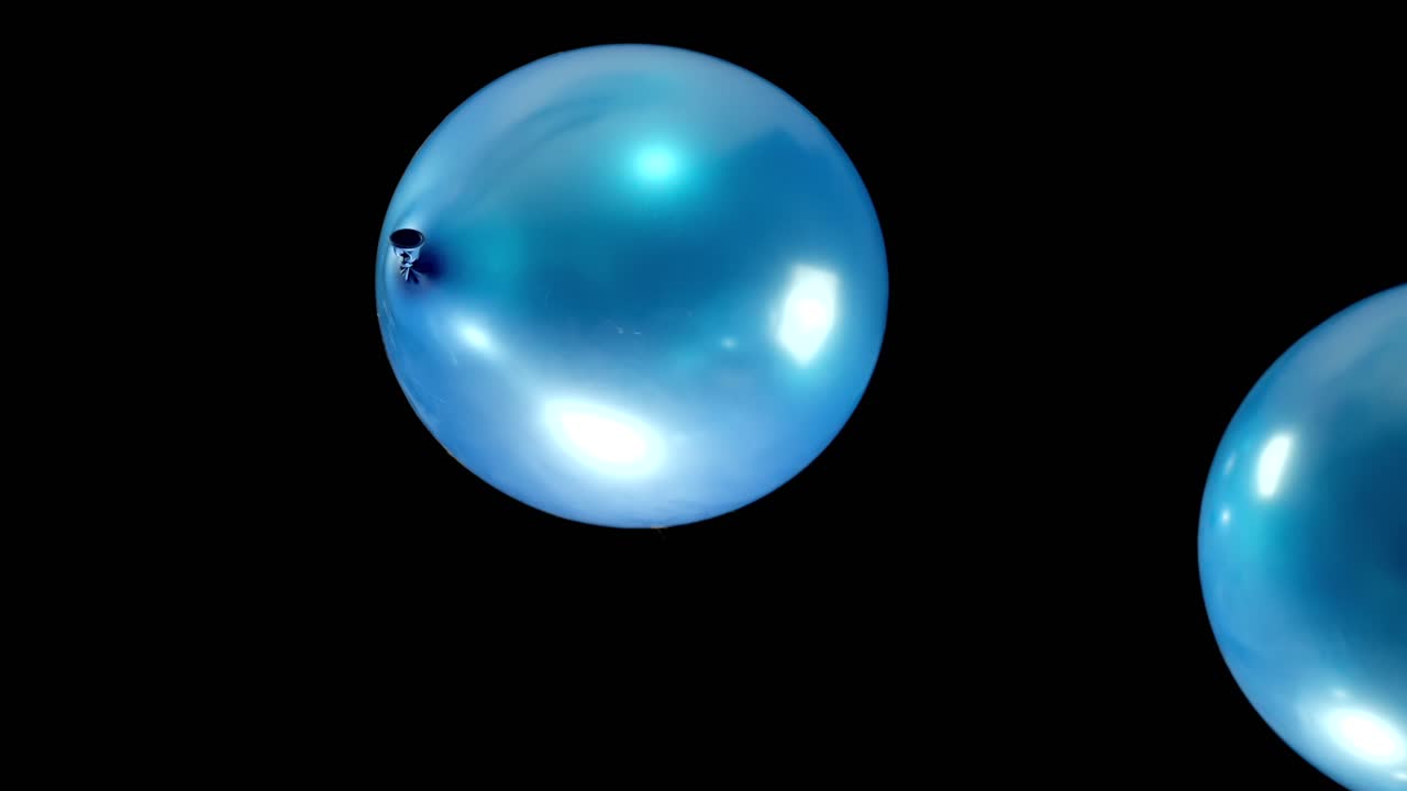 Watch blue shining balloons fall gracefully in slow motion, their shimmering surface catching the light as they gently descend. The peaceful movement creates a mesmerizing and tranquil visual.