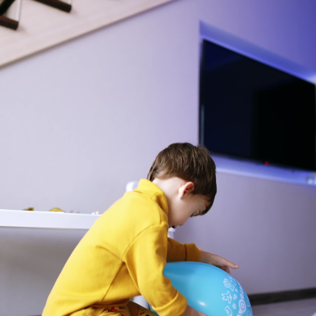 Sweet little kid wearing yellow clothes is at home. Lovely boy takes a big blue balloon to play