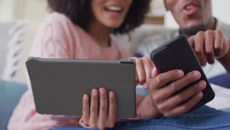 Happy african american couple using tablet and smartphone in living room