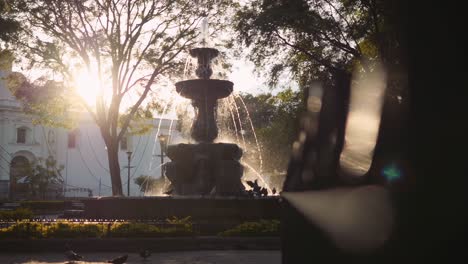 cinematic shot of a pigeon landing on mermaid fountain in guatemala, foreground leading lines and bokeh at sunset