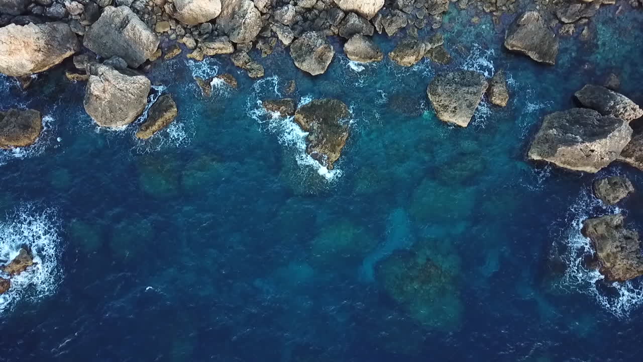 Drone shot of a rocky landscape in Malta, panning downward towards the blue, clear ocean.