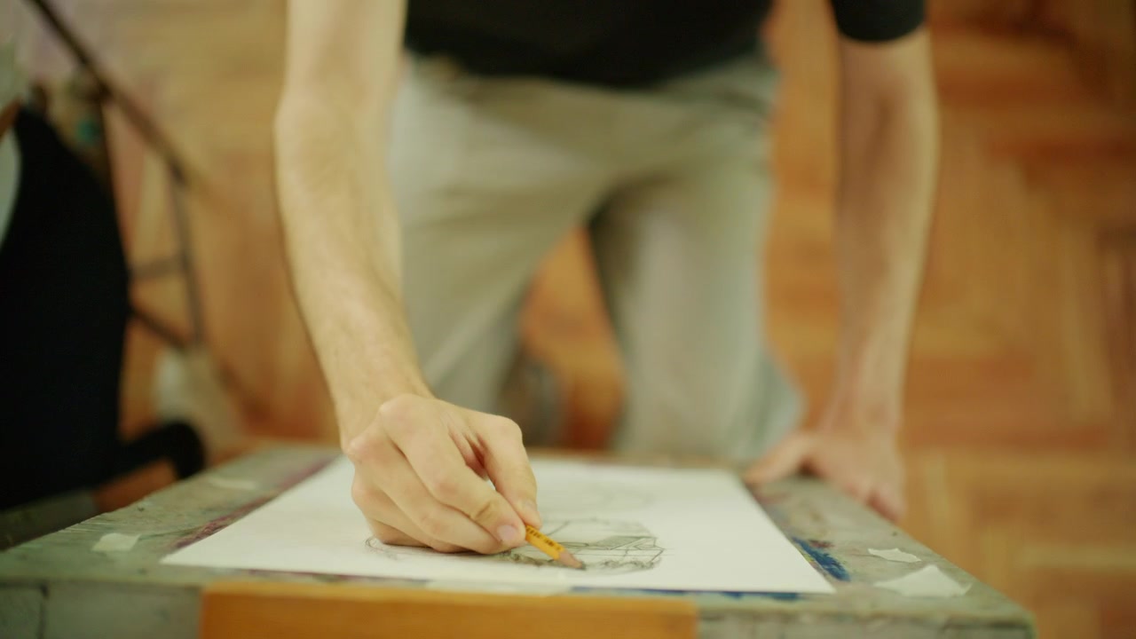 Primo piano della mano di un artista che disegna su carta durante una lezione di disegno