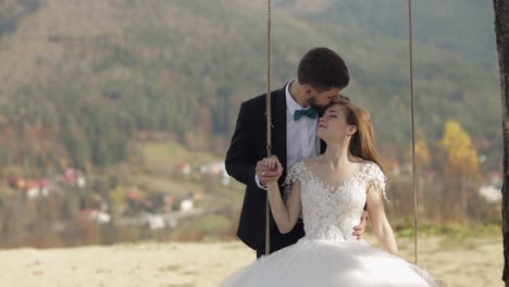 newlyweds. caucasian groom with bride ride a rope swing on a mountain slope