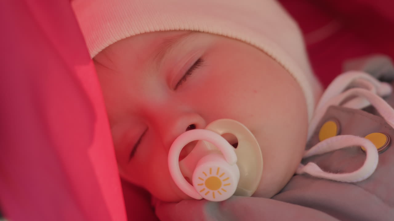 Quiet infant resting. Peaceful infant with pacifier in stroller. Calm baby relaxing with pacifier during family outing. Serene infant enjoying nap under canopy with pacifier and parent nearby
