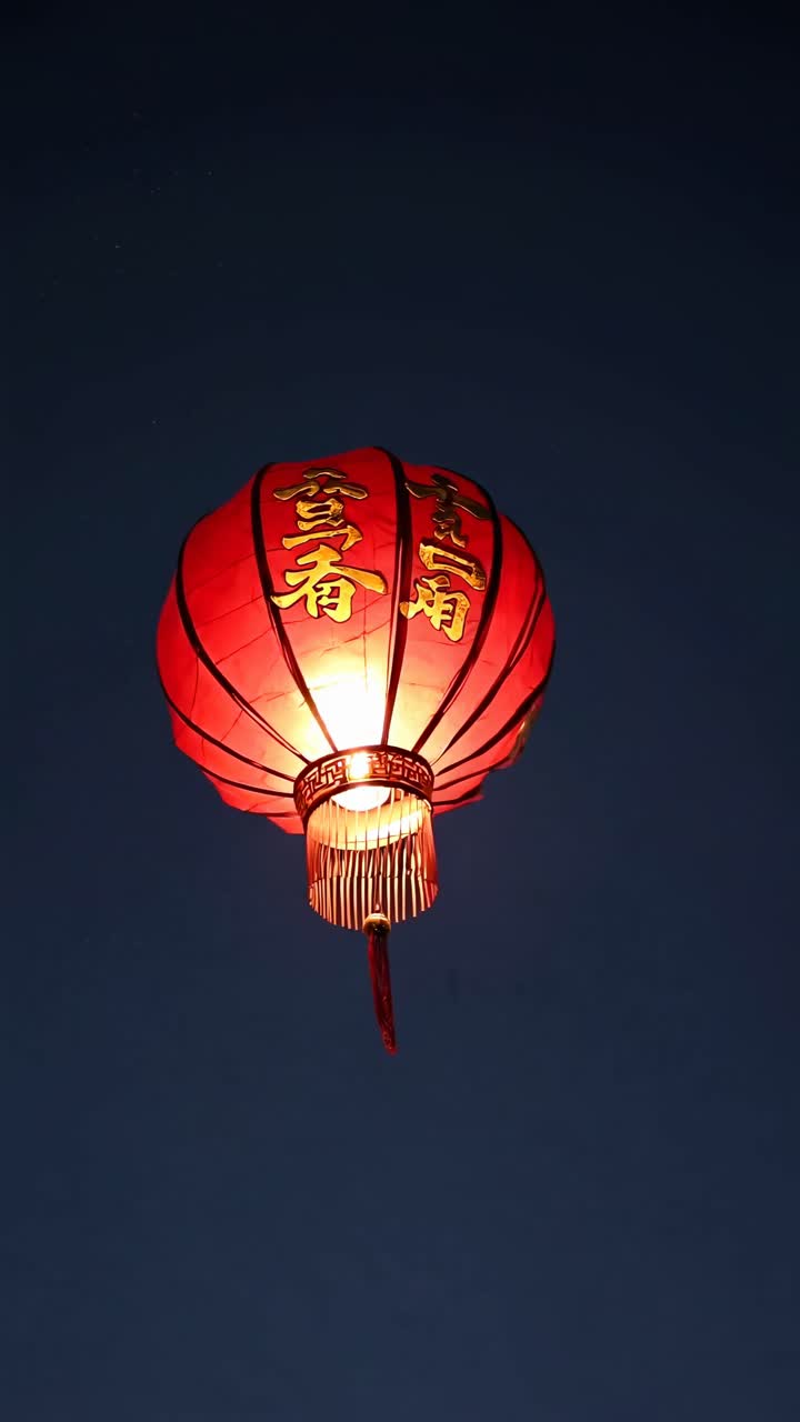 A vibrant red lantern floats against a dark sky, captured from a low-angle