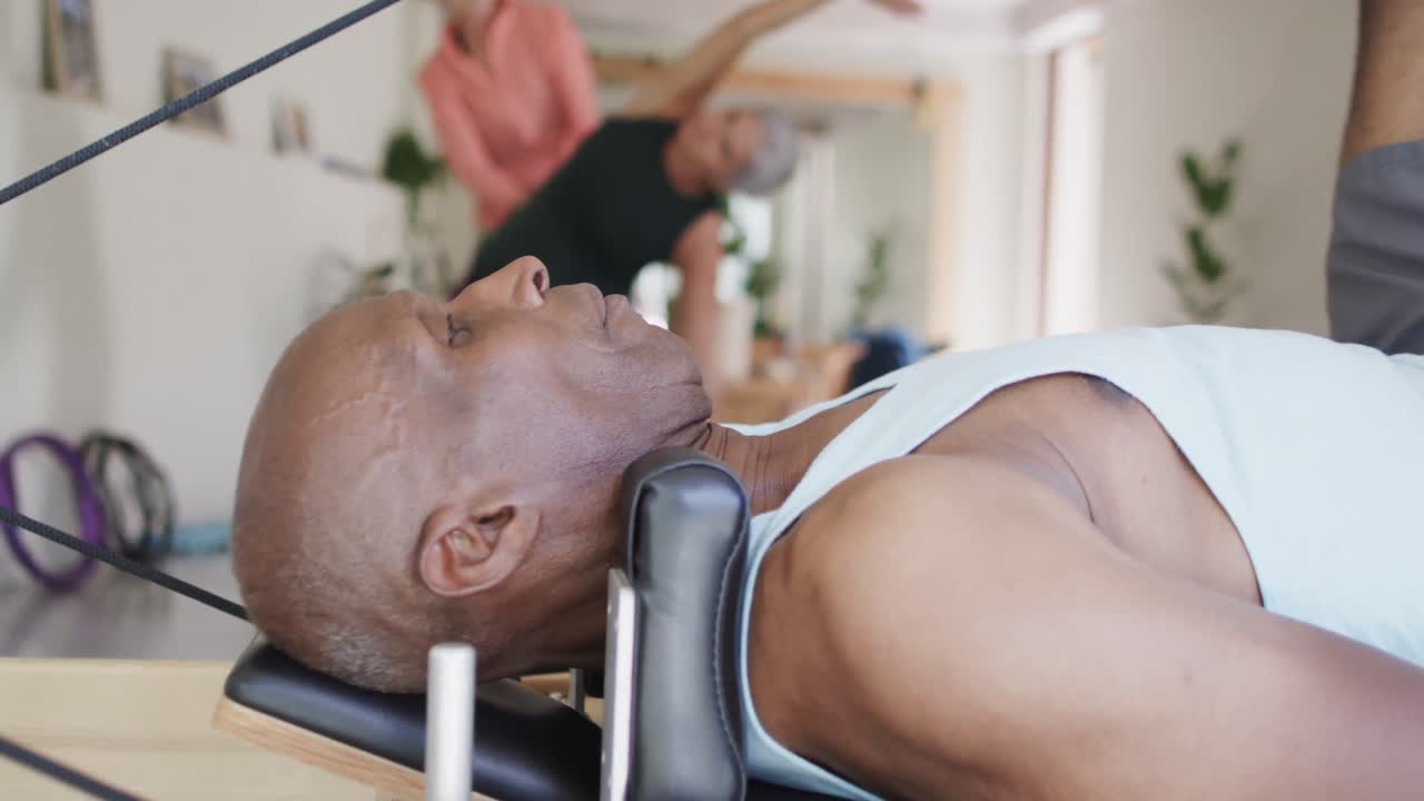 Focused diverse seniors stretching in pilates class with female coach, unaltered, in slow motion