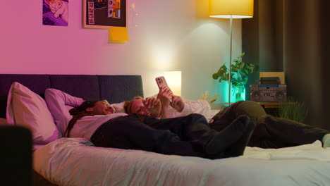 happy couple relaxing in bed together and looking at their phone