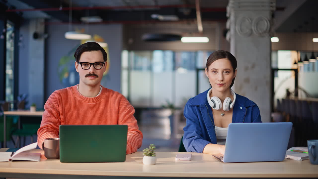 Cheerful coworkers posing camera at company space closeup. Two young startupers