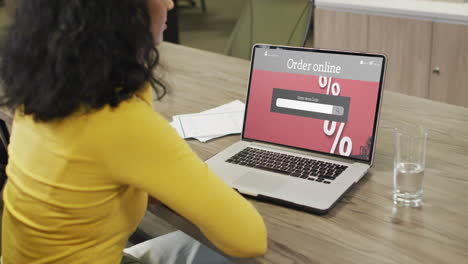 Biracial-woman-at-table-using-laptop,-online-shopping-during-sale,-slow-motion