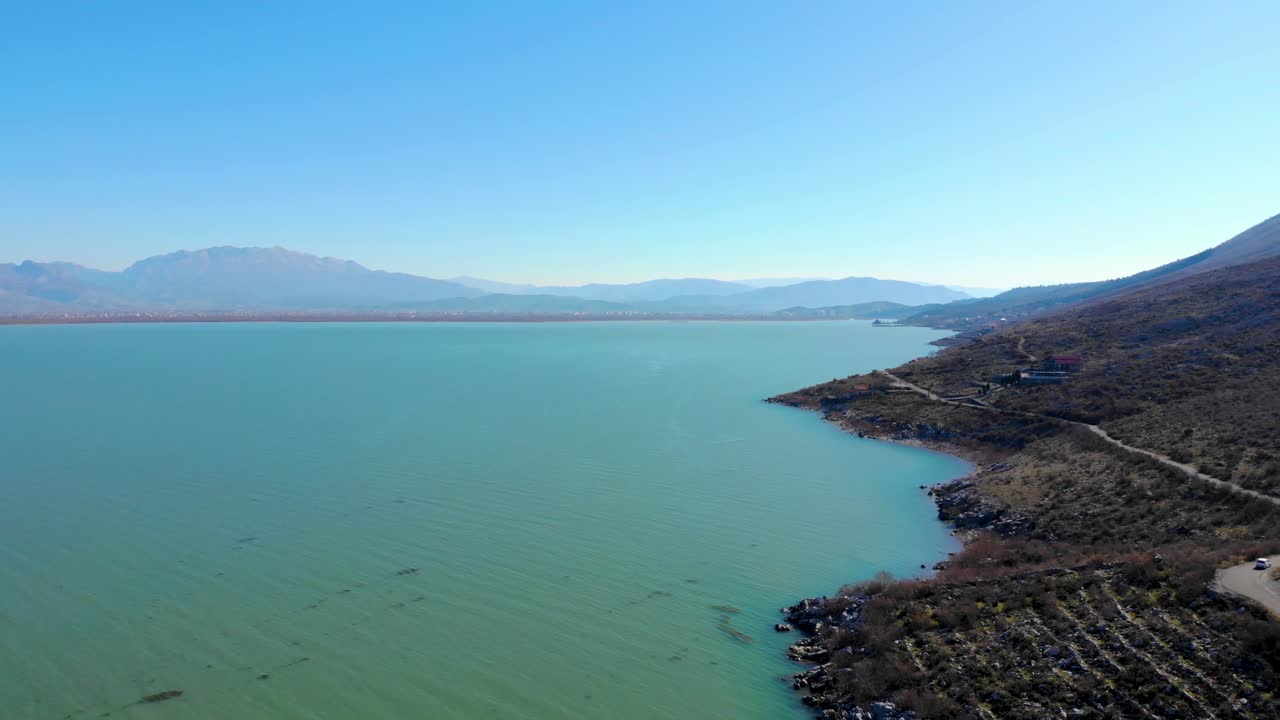 Mountain lake with calm water washing rocky shore with dry bushes on a peaceful landscape in Shkodra