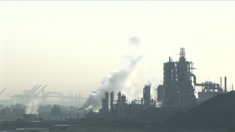 smoke rises from a petrochemical factory or oil refinery under a cloudy sky