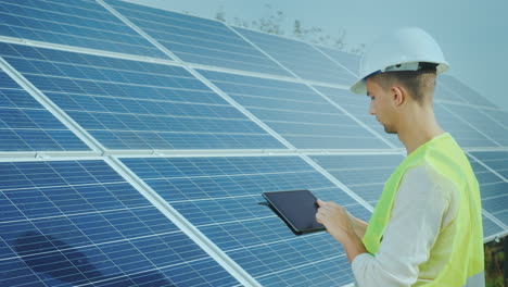 a good-looking worker uses a tablet near ground-based solar panels