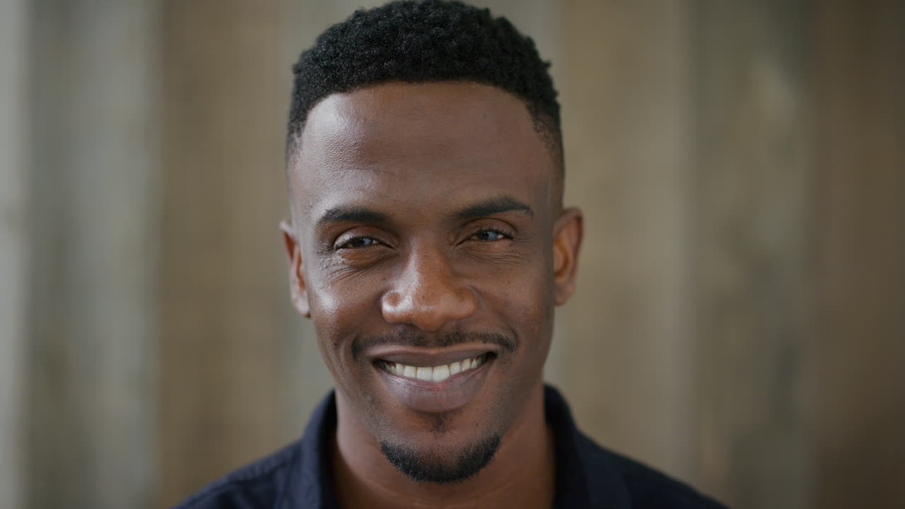 retrato de cerca de un joven afroamericano guapo sonriendo confiado disfrutando de un estilo de vida exitoso con camisa negra en cámara lenta