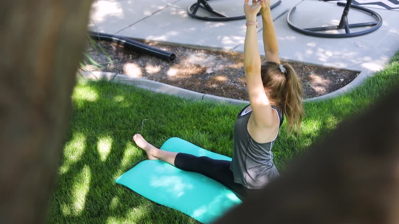 toma en cámara lenta panorámica desde detrás de un árbol y revelando a una mujer haciendo yoga en una alfombra de yoga