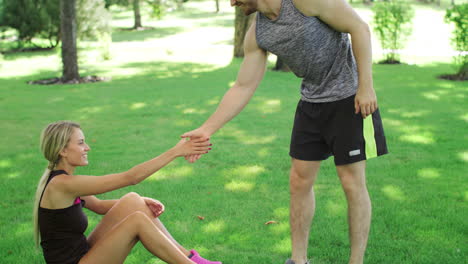 athlete man help young woman stand up from green lawn. sport people teamwork