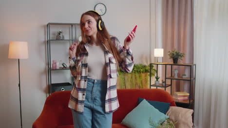 pretty caucasian young woman in headphones listening music dancing, singing in living room at home