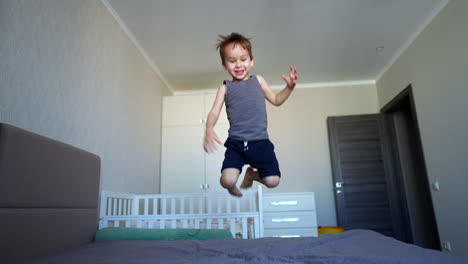 happy caucasian toddler boy jumps on the big bed. kid falls on the bed and moves his arms and legs.