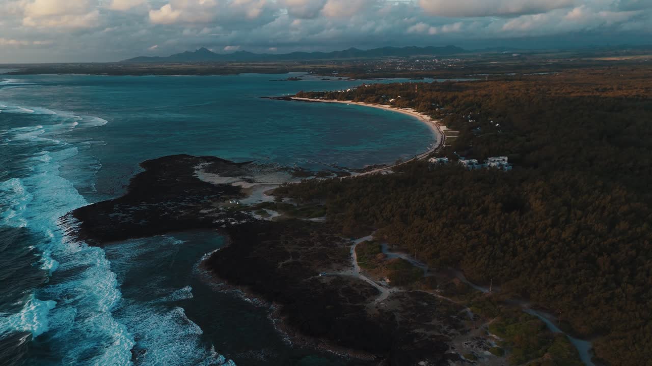 Aerial of coastline at sunrise with blue ocean and rocky shore under warm morning light