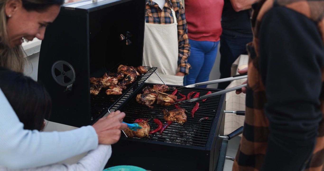 Famiglia e amici felici che grigliano pollo e peperoni su un barbecue