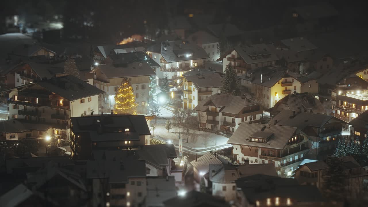 A serene winter night in the Alps with cozy lights glowing over snow-covered houses and trees.