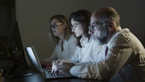 tired business people with laptops in dark office