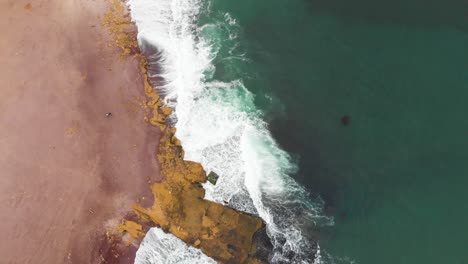 Tilt-up-shot-of-waves-breaking-at-the-coast-line-of-the-Red-Beach,-to-tourists-walking-in-the-desert