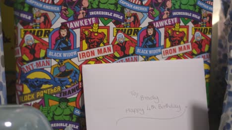 a shot close up and panning across of a young boys birthday presents. this includes presents wrapped in spotty blue paper, football paper and marvel super heros.