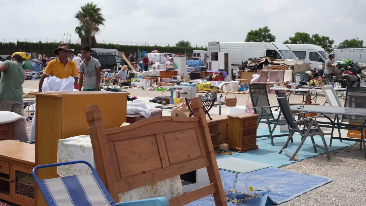 A bustling open-space flea market displays household items, including reusable furniture, as shoppers browse and explore the eclectic selection of goods.