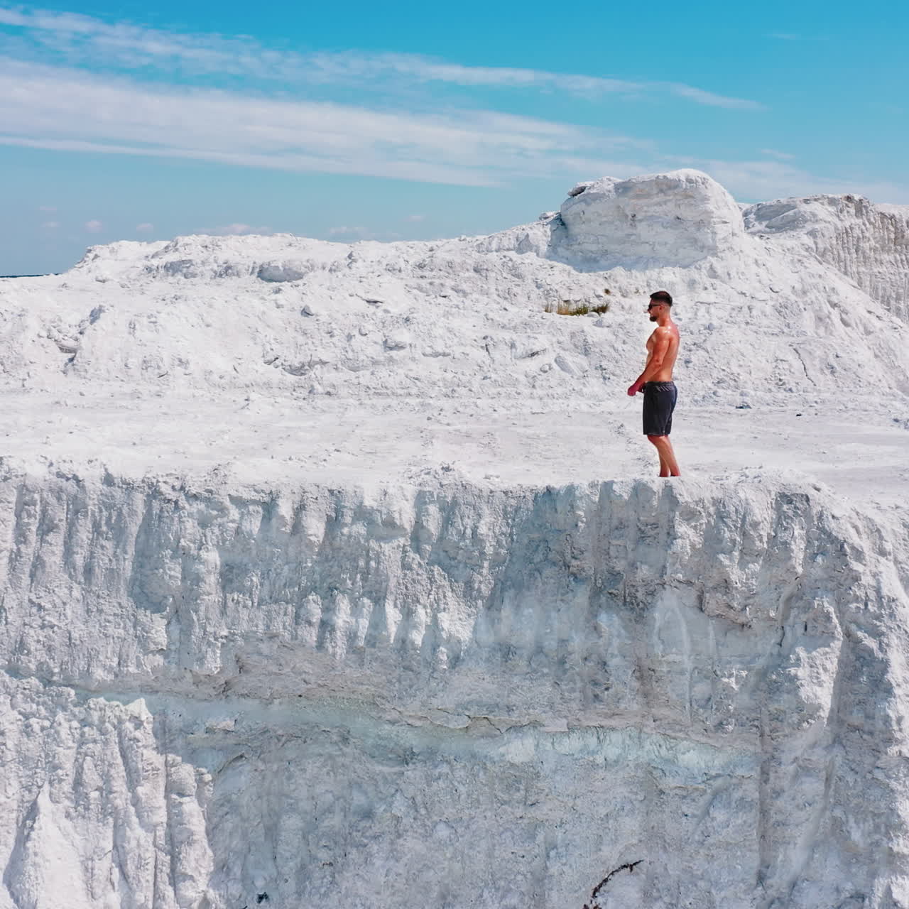 Young sporty man in white mountains. Healthy man without shirt walking along rocky canyon in a warm sunny day. Aerial view.