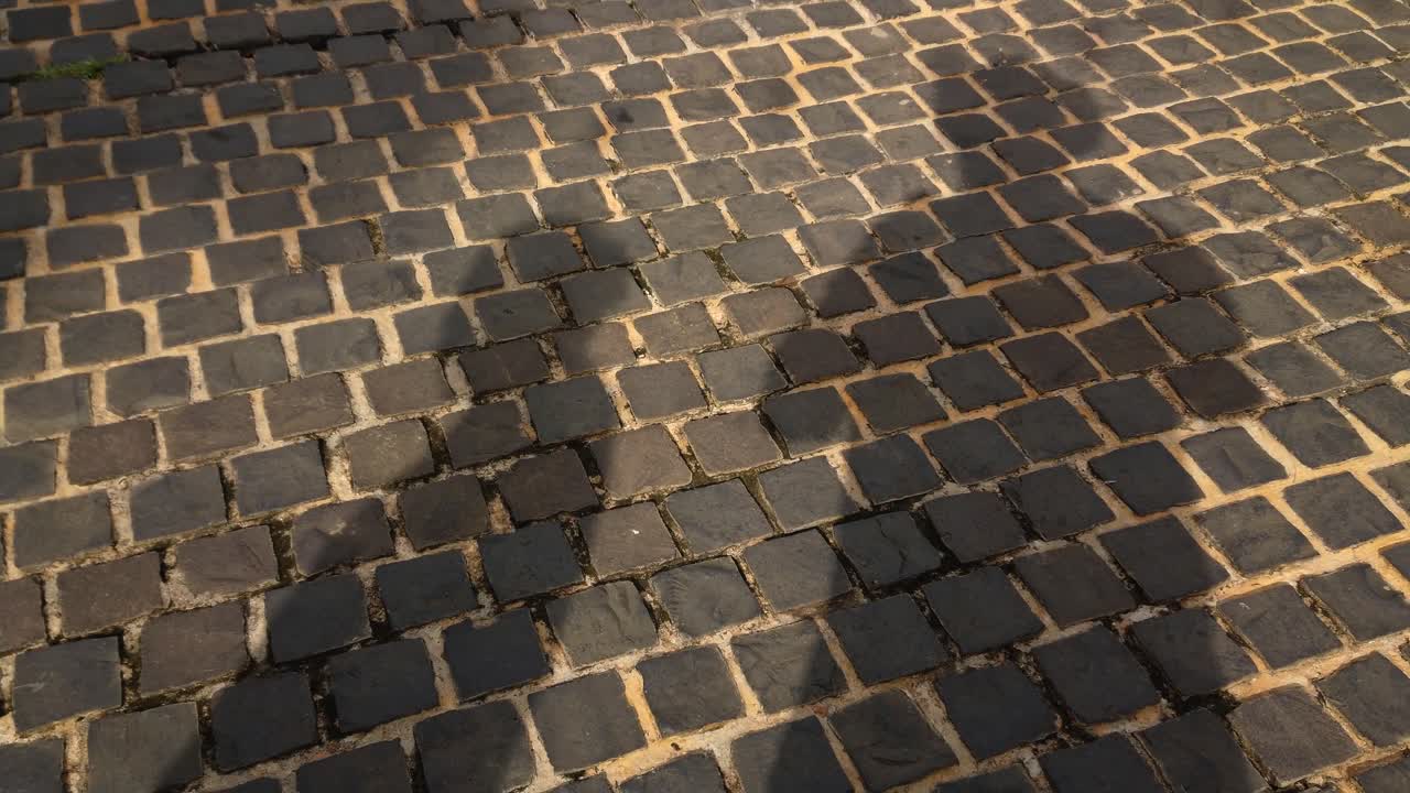 다른 사람들이 지나갈 때 자신의 그림자를 드리우면서 벽돌로 된 포장 도로에 서서 자신의 그림자를 드리우는 남자