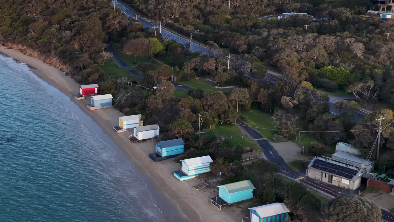Drone glides above vibrant bathing boxes along Rye beach at dusk, capturing tranquil coastal scenery