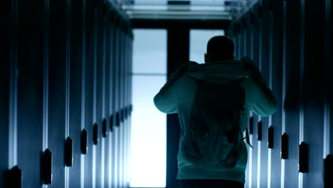 Back View of a Hacker Putting on his Hoodie and  Walking Through Data Center Corridor,