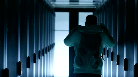 back view of a hacker putting on his hoodie and  walking through data center corridor,