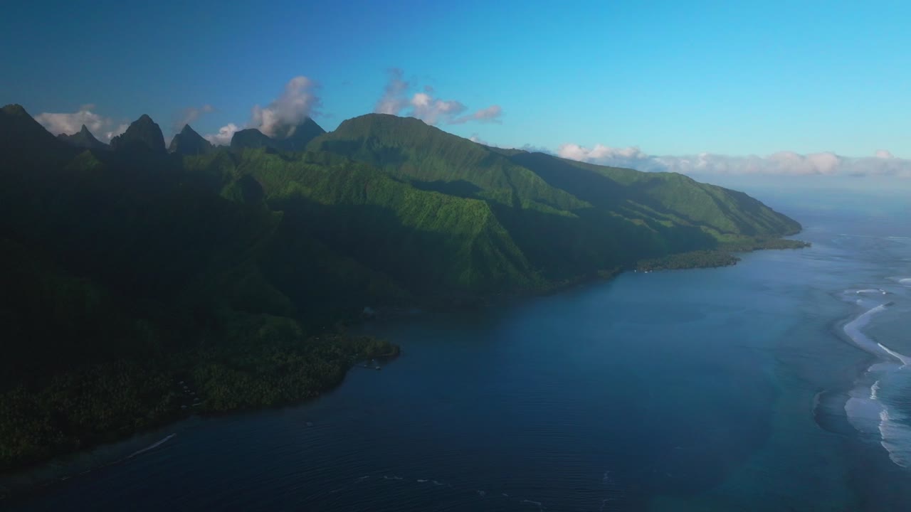 Hazy sunset last light coastline volcano island mountain valley peaks village Teahupoo Tahiti aerial drone French Polynesia afternoon coral reef surfer Paris 2024 Summer Olympics venue backward motion