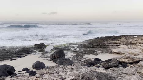 The-powerful-waves-of-the-Pacific-Ocean-crash-against-the-rugged-rocky-shoreline-at-dusk-in-Oahu,-Hawaii