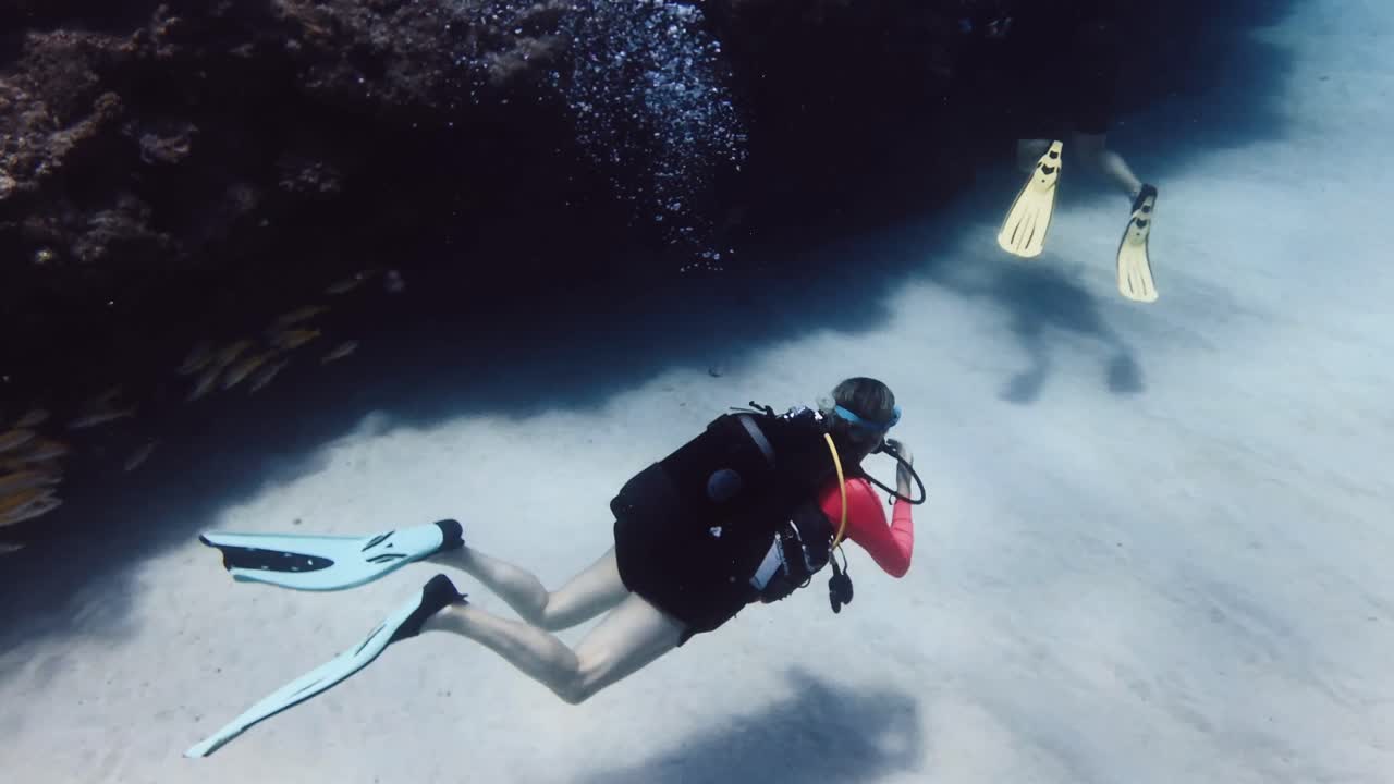 Due subacquei esplorano lentamente il fondale sabbioso lungo una parete corallina nelle acque limpide di Mauritius. Scena di viaggio subacqueo pacifica ideale per il turismo subacqueo, l'esplorazione marina e l'avventura oceanica